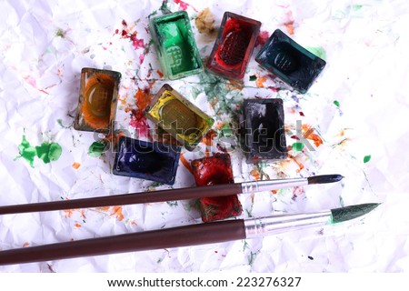 Watercolor paint cubes with brushes and spilled paint on white paper background