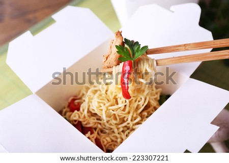 Chinese noodles and sticks in takeaway box on mat background