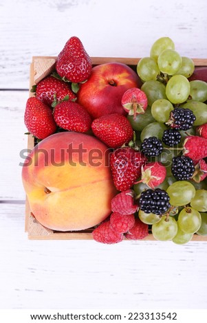 Different berries and fruits in box on wooden table close-up