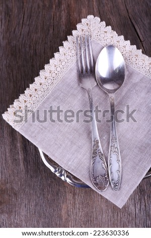 Metal spoon and fork on lace napkin on metal plate on wooden background