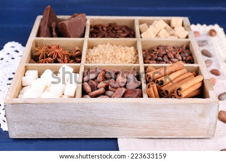 Wooden box with set of coffee and cocoa beans, sugar cubes, dark chocolate, cinnamon and anise on wooden background