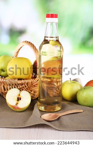 Apple cider vinegar in glass bottle and ripe fresh apples, on wooden table, on nature background