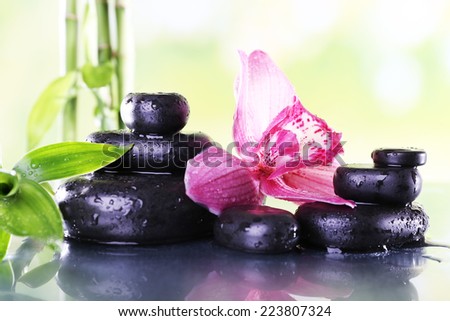 Spa stones, bamboo branches and lilac orchid on table on natural background