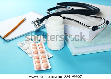 Medical stethoscope with books and tablet on blue background
