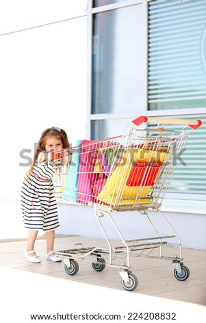Happy little girl with shop bags in supermarket trolley, outdoors