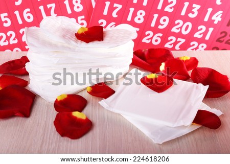 Sanitary pads and rose petals on wooden table on calendar background