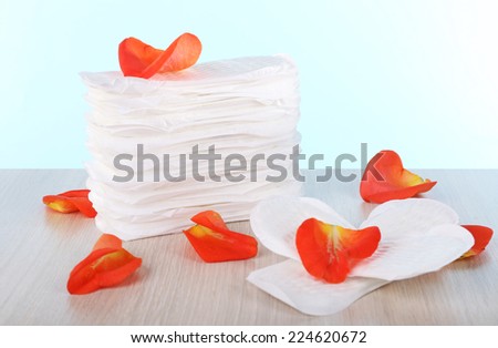 Sanitary pads and rose petals on wooden table on light blue background