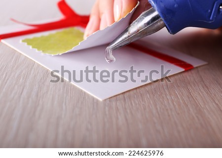 Woman\'s hand making postcard with red ribbon and bow with a help of glue gun