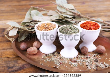 Small round tea bowls with different seasoning and bay leaves on a metal round tray on wooden background