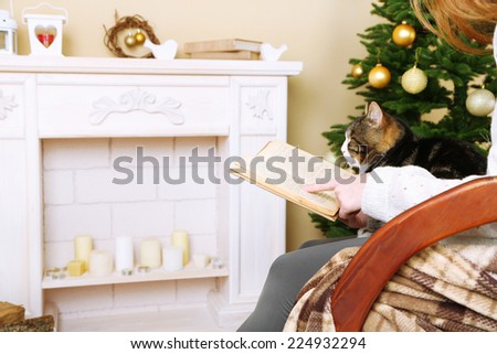 Woman and cute cat sitting on rocking chair and read the book in the front of the fireplace