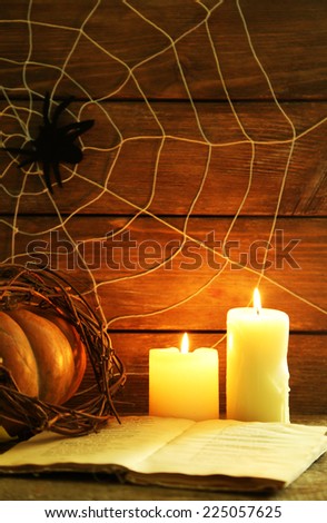 Halloween decoration with spider on web, book, pumpkin and candles on wooden background