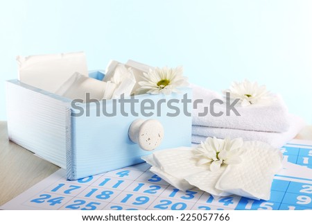 Sanitary pads in box and sanitary pads and white flowers on blue calendar on light blue background