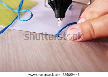 Woman\'s hand making postcard with blue ribbon and bow with a help of glue gun
