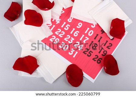 Sanitary pads and rose petals on red calendar on light grey background