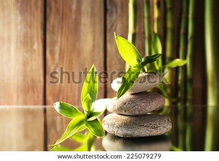 Spa stones and bamboo branches on mirror surface on wooden wall background