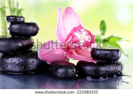 Spa stones, bamboo branches and lilac orchid on table on natural background