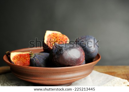 Ripe sweet figs in bowl on wooden table, on dark background