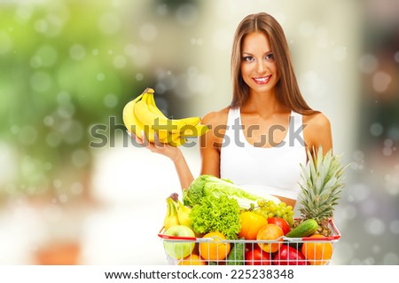 Shopping concept. Beautiful young woman with fruits and vegetables in shopping basket on shop background