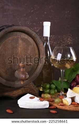 Supper consisting of Camembert cheese, wine and grapes on cutting board and wine barrel on wooden table on brown background