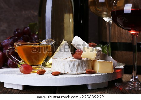 Supper consisting of Camembert cheese, honey, wine and grapes on stand and wine barrel on wooden table on brown background