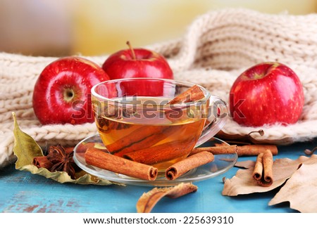 Composition of  apple cider with cinnamon sticks, fresh red apples, warm scarf and autumn leaves on wooden table, on bright background