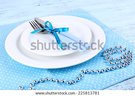 White plates, fork, knife and Christmas decoration on blue polka dot napkin on wooden background
