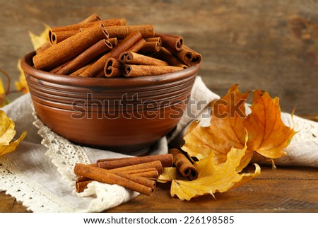 Cinnamon sticks in bowl with yellow leaves on wooden background
