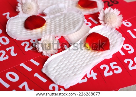 Sanitary pads, white Berbers and rose petals on red calendar background