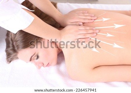 Back massage. Beautiful young woman having back massage in spa salon  (with arrows)