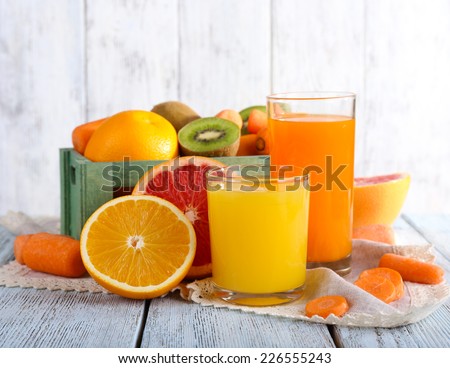 Fruit and vegetable juice in glasses and fresh fruits in box on wooden table on wooden wall background