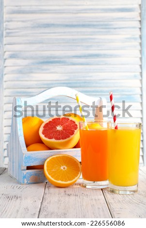 Orange and carrot juice in glasses and fresh fruits in wooden box on wooden table on wooden wall background