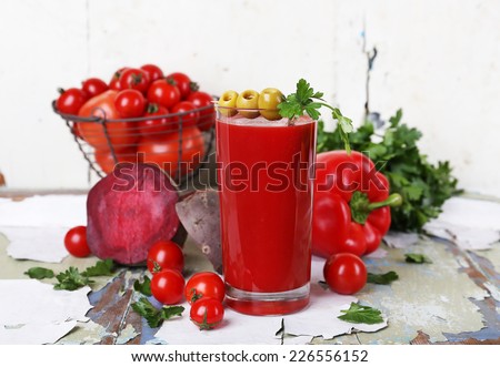 Glass of tomato juice and fresh vegetables on old wooden table on wall background