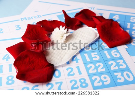 Sanitary pads, white Berber and rose petals on red calendar background
