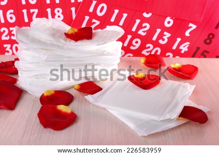 Sanitary pads and rose petals on wooden table on calendar background