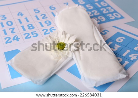 Sanitary pads, calendar and white flower on light blue background