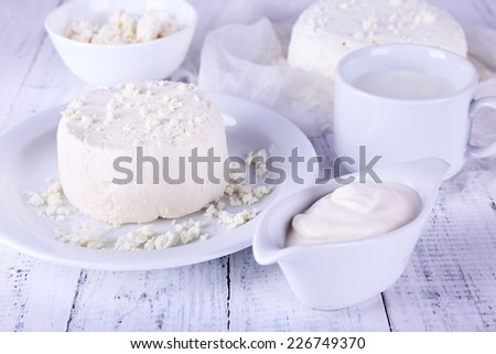 Cottage cheese on plate on gauze and cottage cheese in bowl, cup of milk and cream in saucer boat on wooden background