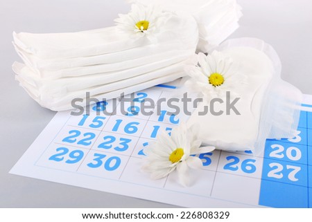 Sanitary pads, calendar and white flowers on light background