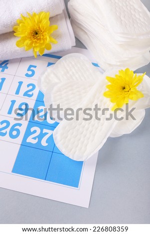 Sanitary pads and yellow flowers on blue calendar background