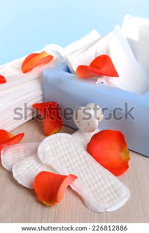 Sanitary pads in box and rose petals on wooden table on light blue background