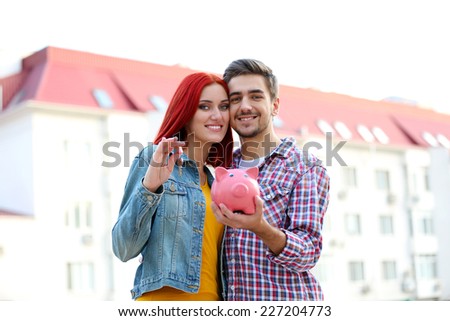 Loving couple with piggy bank near apartment house
