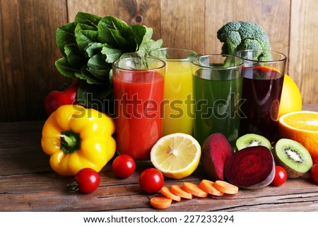 Fruit and vegetable juice in glasses and fresh fruits and vegetables on wooden table on wooden wall background