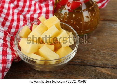 Raw peeled and chopped potatoes in glass bowl and bottle with olive oil on wooden background
