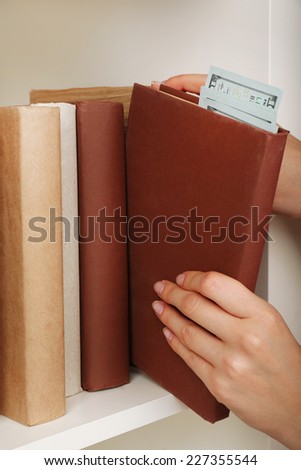 Woman hiding money in book at home