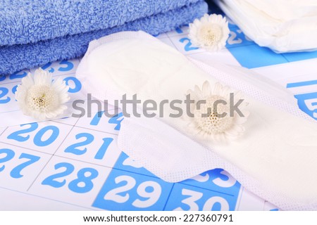 Sanitary pads, white flowers and towel on blue calendar background
