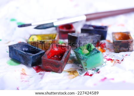 Watercolor paint cubes with brushes and spilled paint on white paper background