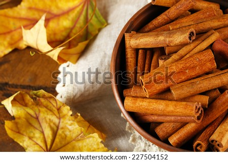 Cinnamon sticks in bowl with yellow leaves on wooden background