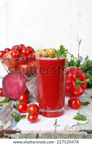 Glass of tomato juice and fresh vegetables on old wooden table on wall background