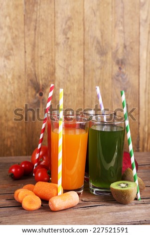 Fruit and vegetable juice in glasses and fresh fruits and vegetables on table on wooden background