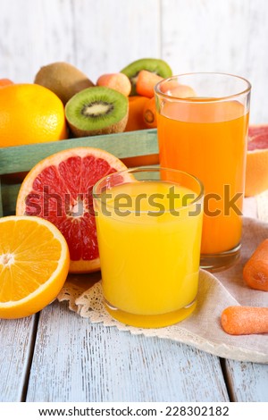 Fruit and vegetable juice in glasses and fresh fruits in box on wooden table on wooden wall background