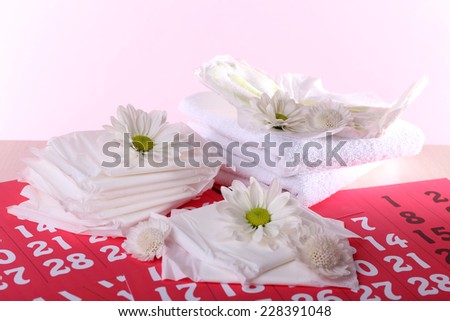 Sanitary pads and white flowers on red calendar on pink background